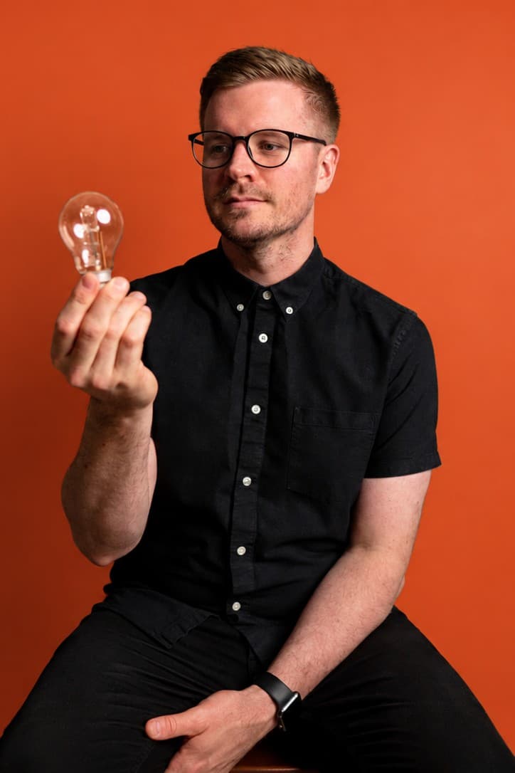 Shane Michael Hatton holding a lightbulb, on an orange background